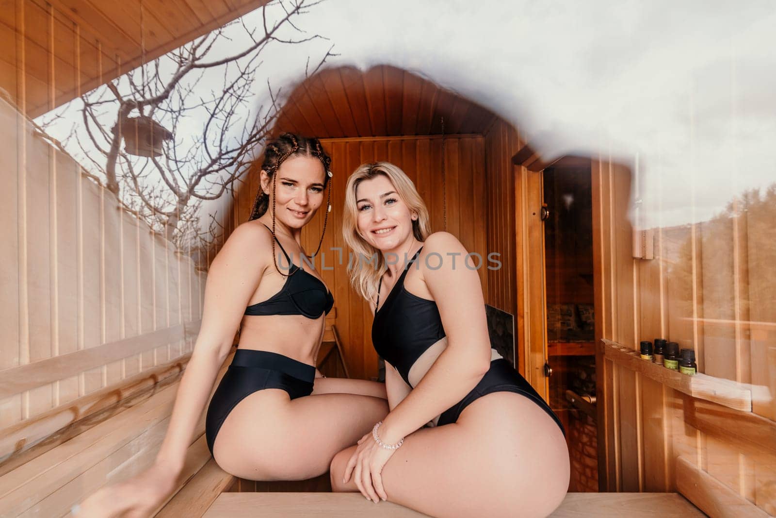 Sauna friend. Two women are sitting in a sauna in black bathing suits and talking to each other. by Matiunina