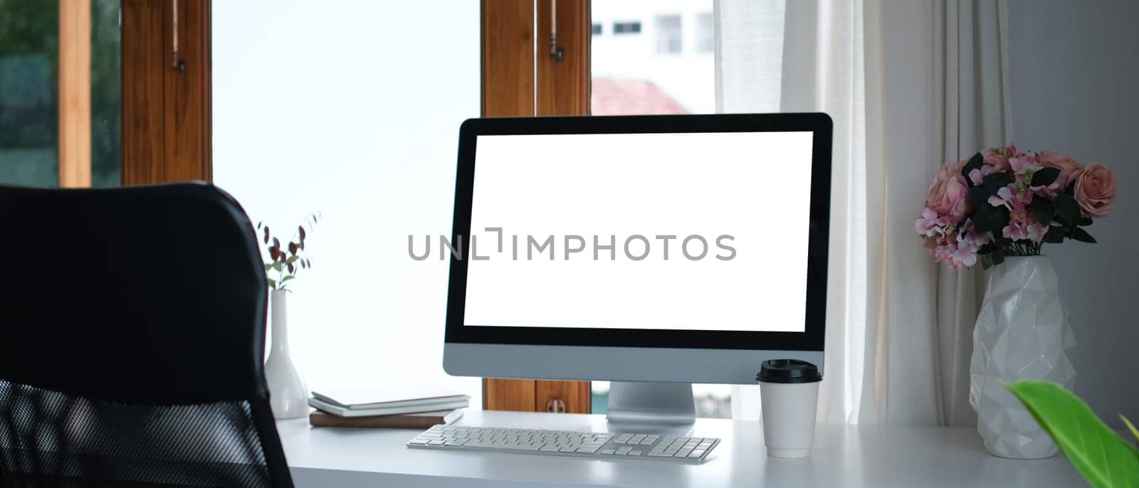 Blank computer monitor, pink roses in vase and books on white table. Empty screen for your advertising text message.