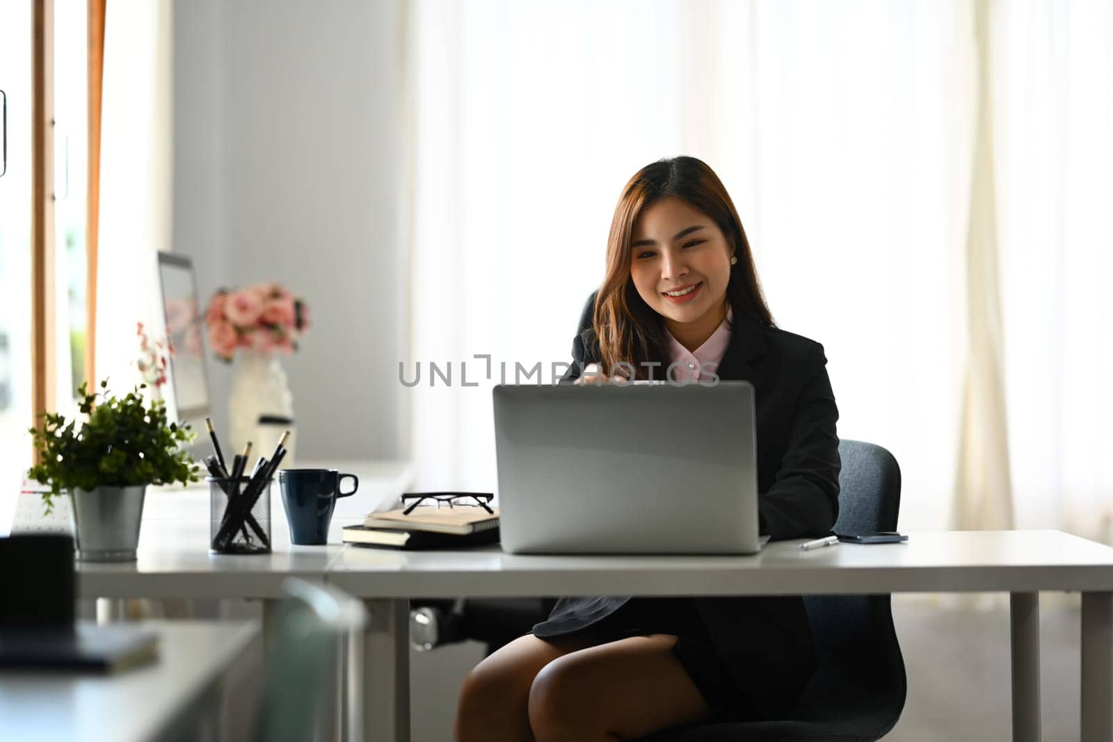 Portrait of millennial female secretary sitting in modern workplace and using laptop computer.