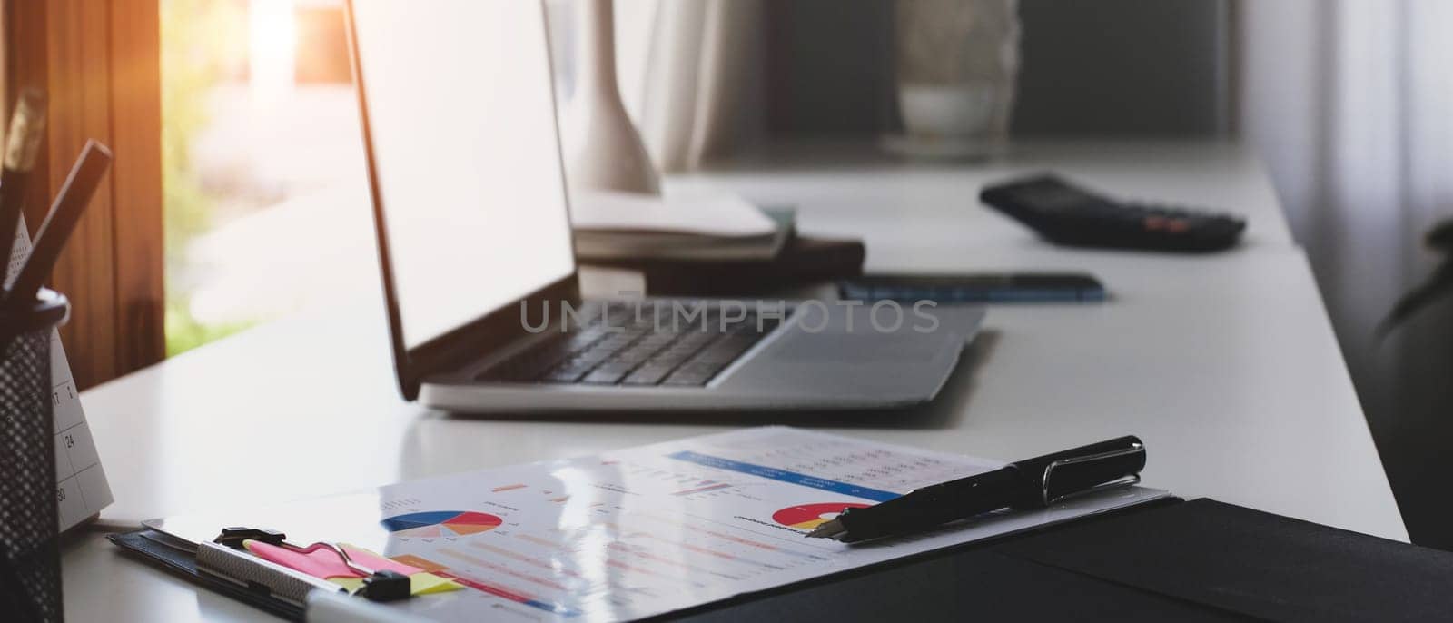 Side view of laptop computer, financial reports and office supplies on white office desk.