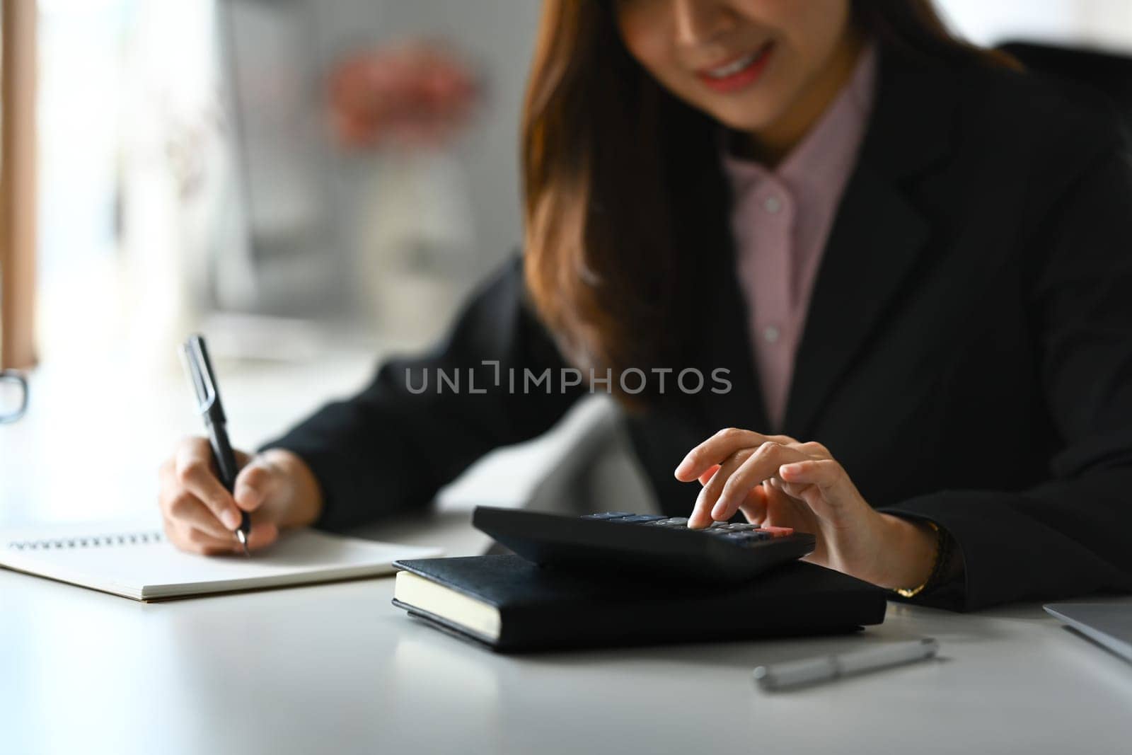 Professional female accountant using calculator to check company finances income and budget at office desk.
