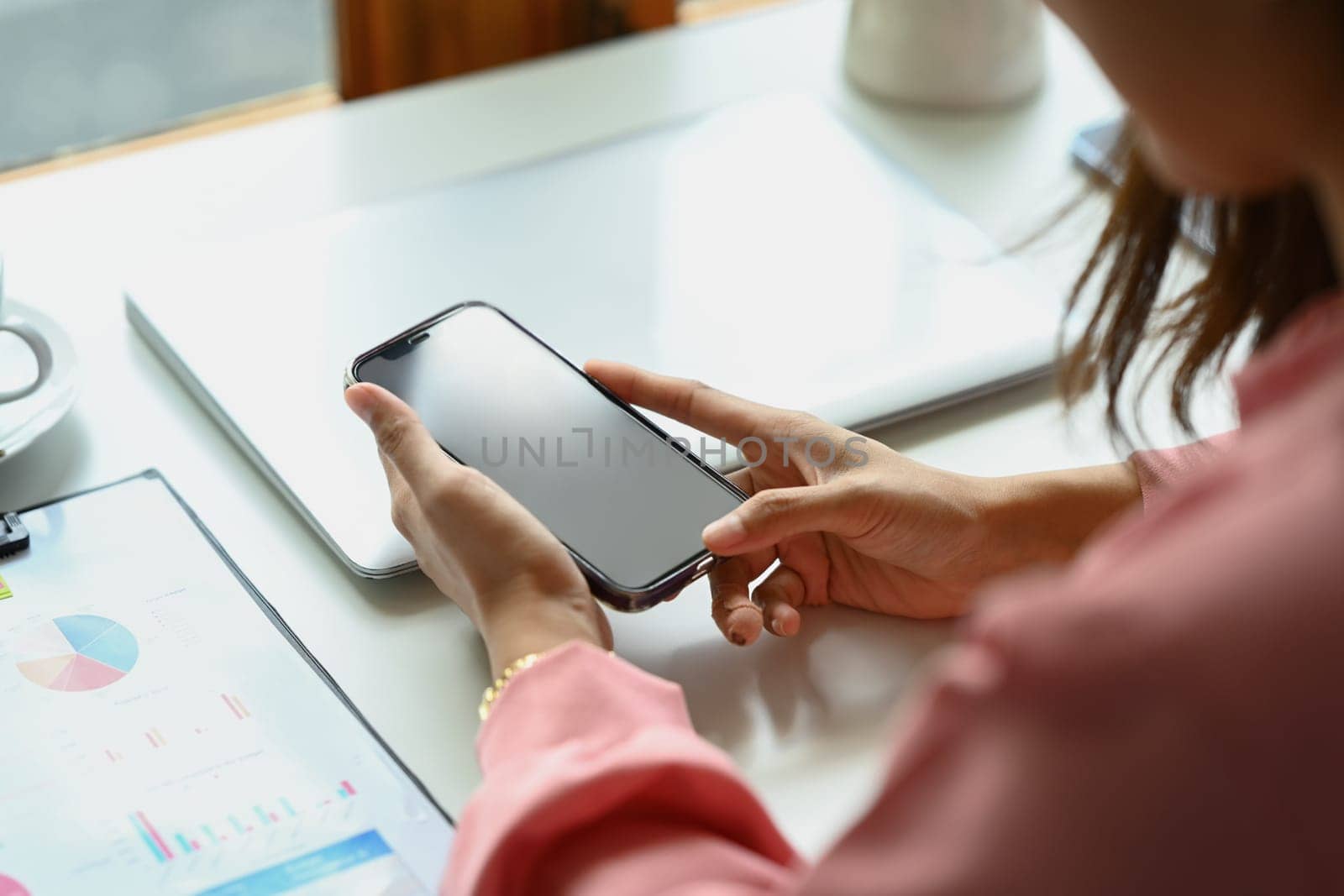Closeup view shot young woman sitting at her office desk and using smartphone by prathanchorruangsak