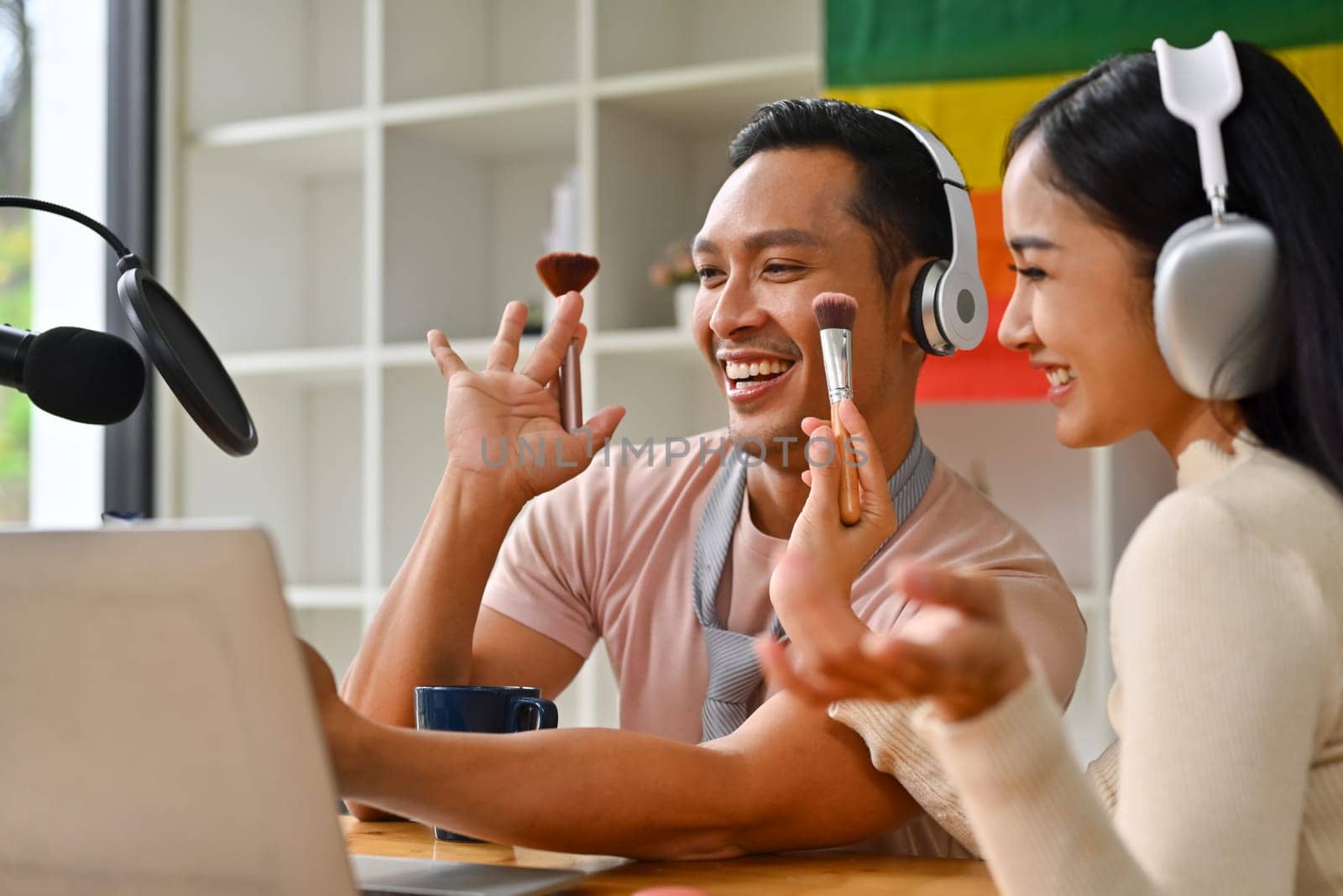 Attractive young gay man and woman using laptop and microphone streaming audio podcast at home studio.