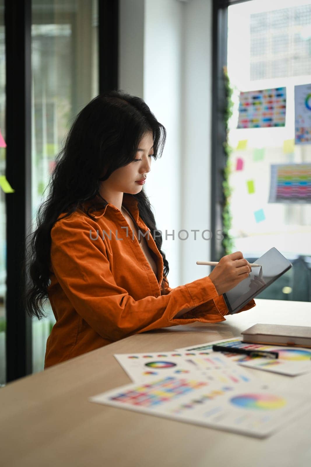 Pretty Asian female graphic designer drawing something on digital tablet working on new design project at creative office.