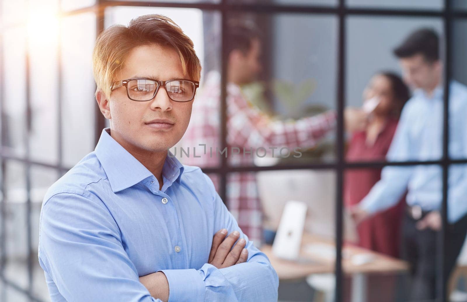 Portrait of a confident young businessman standing with his arms crossed in an office. by Prosto