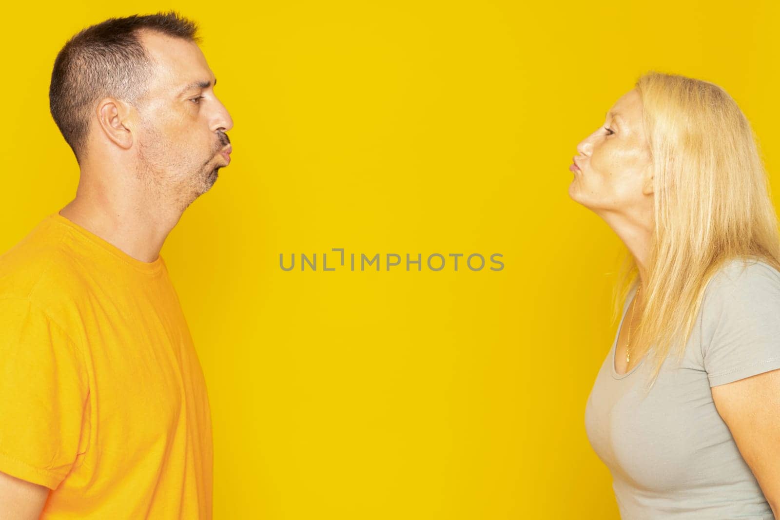 Caucasian couple in their 40s blowing a kiss with their eyes closed as a sign of mutual love and affection isolated on yellow studio background