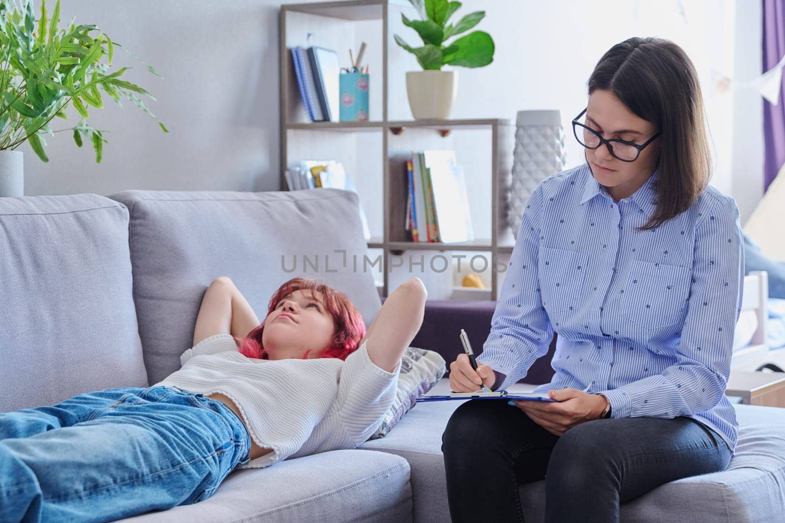 Psychologist helping teenage female, individual therapy in doctors office. Professional counselor listening teenager, girl lying on couch. Mental health, adolescence, psychology, psychiatry concept