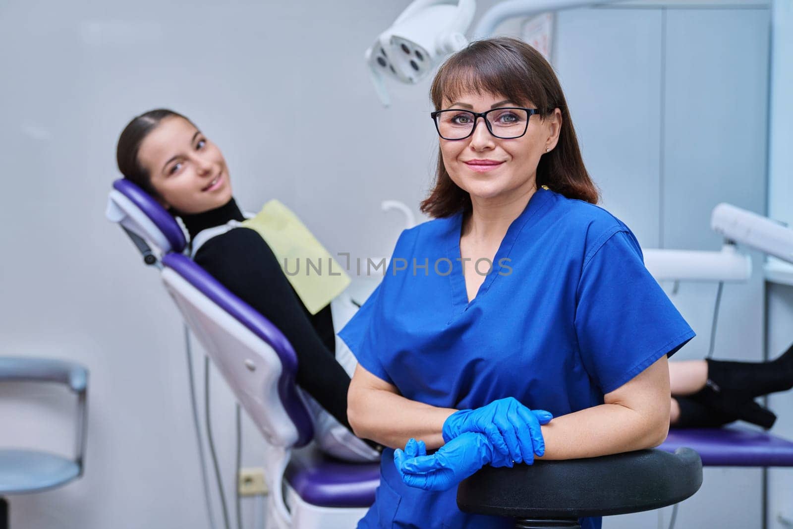 Portrait of female dentist with girl patient sitting in dental chair by VH-studio