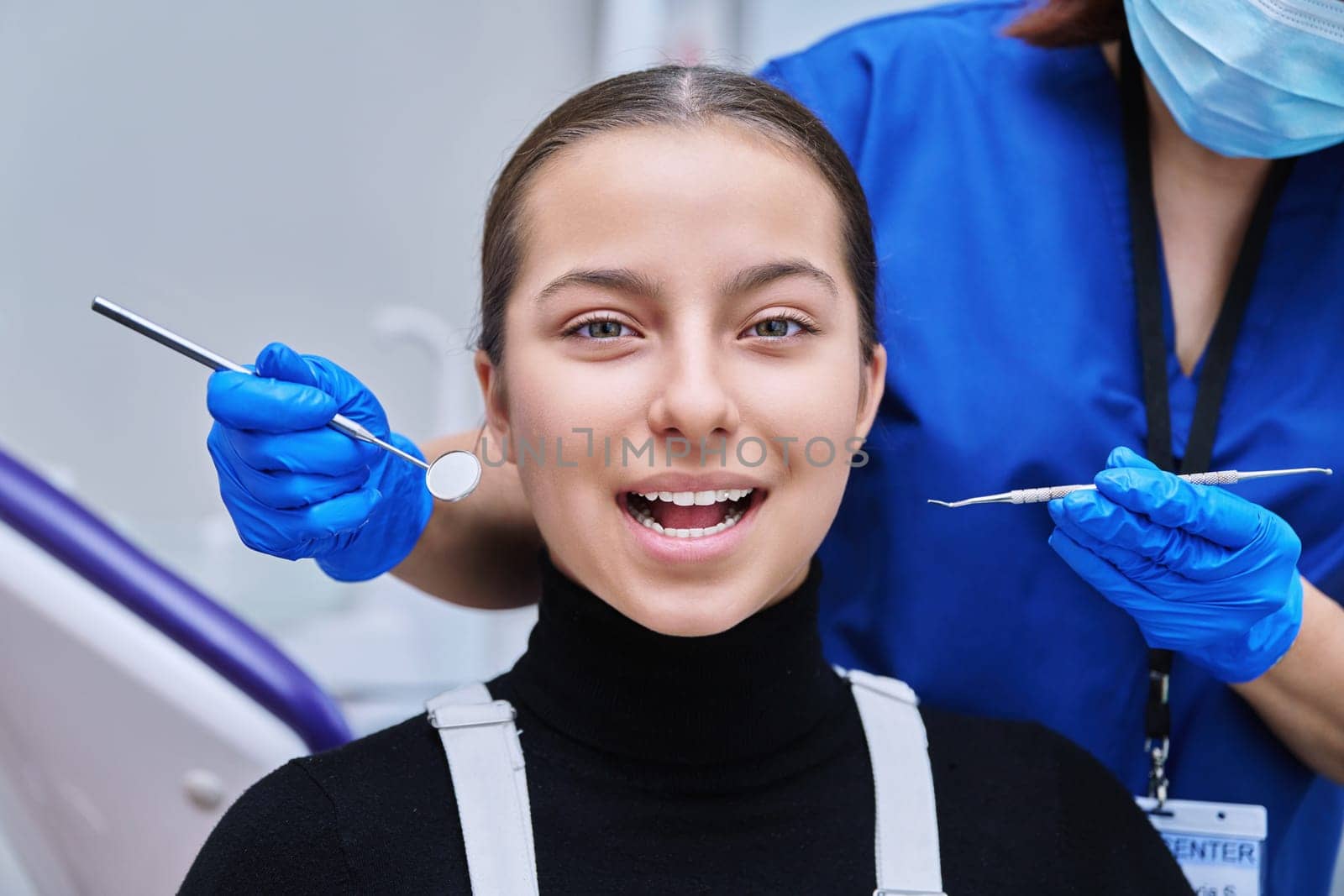 Young teenage female at dental examination treatment checkup in clinic. Teen girl sitting in chair doctor dentist with tools examining patient teeth. Adolescence hygiene dentistry dental health care