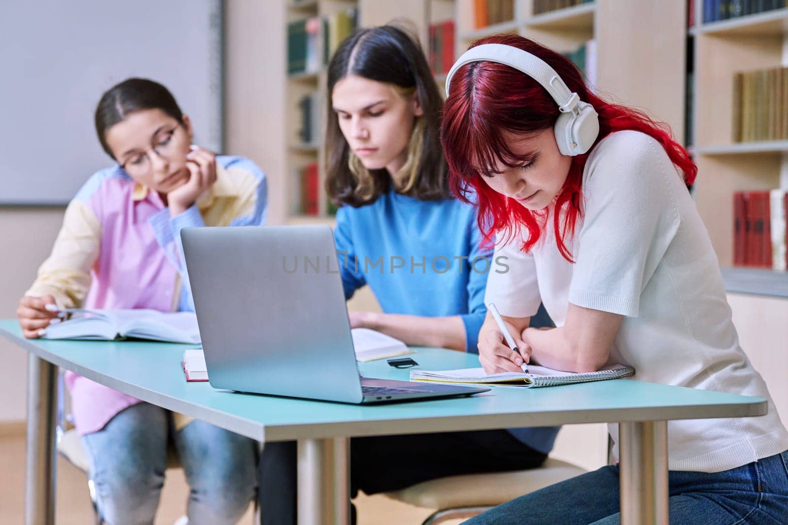 Group of teenage students study at their desks in library class. Teen students writing in notebooks using books laptop. Education, knowledge, high school, college concept