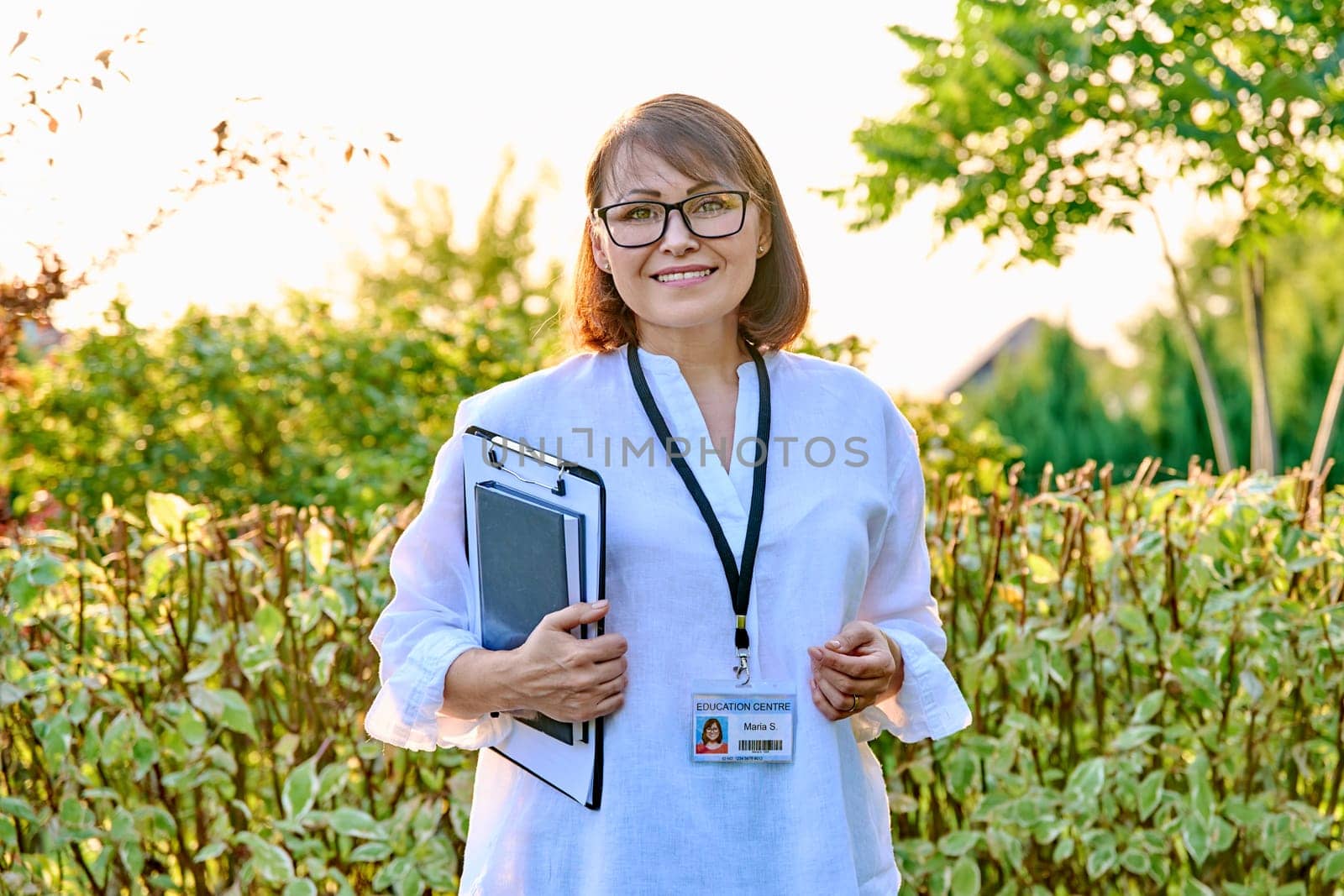 Outdoor portrait of female teacher with clipboard badge. Middle aged female mentor, educator, psychologist, social worker, counselor smiling looking at camera