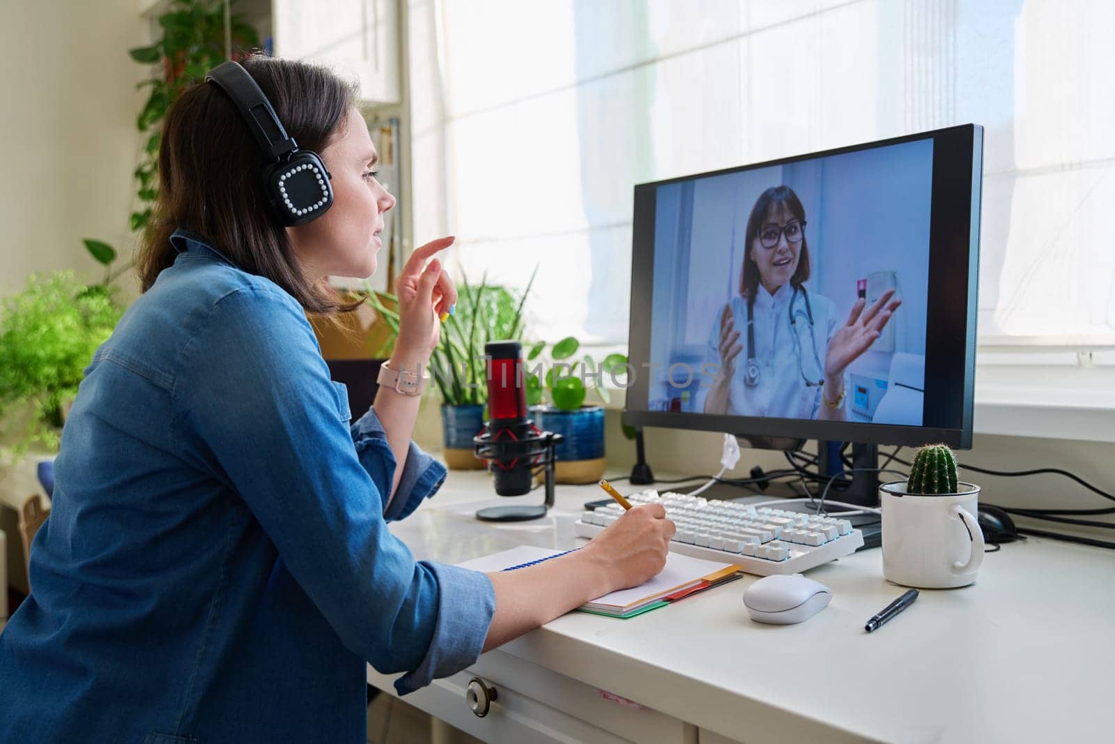 Young woman having a video conference with a doctor. Female patient sitting at table at home talking with general practitioner. Technology, medicine, online consultation, health care concept