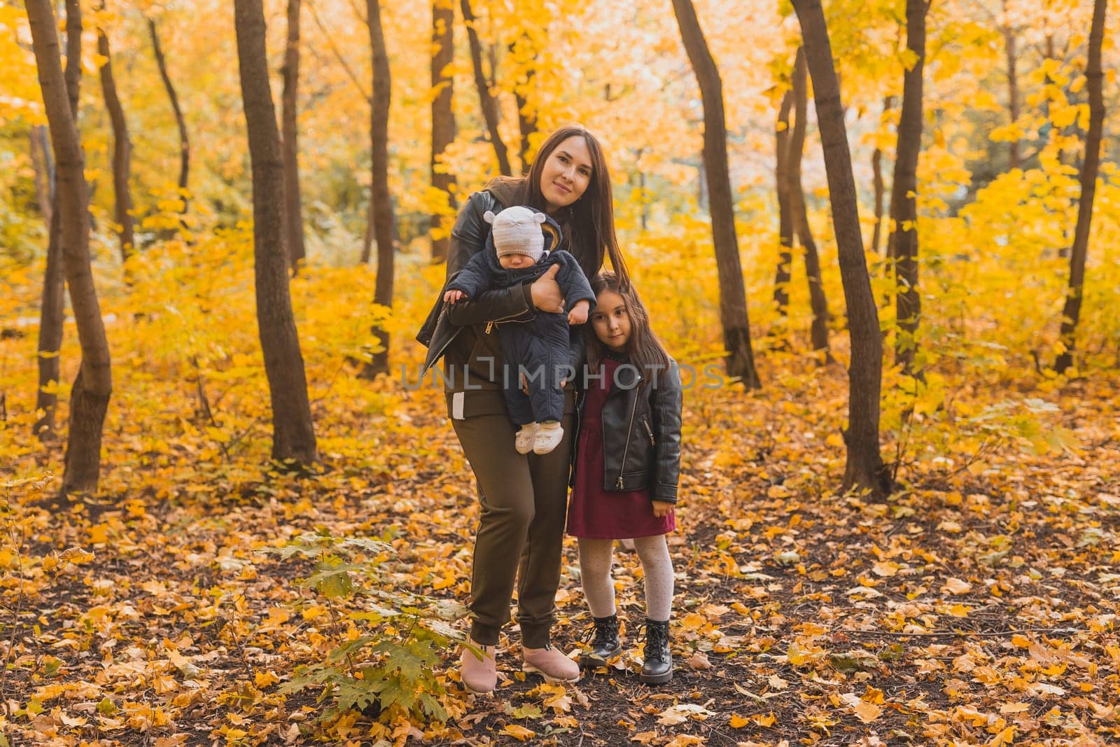 Caucasian mother with glasses is playing in leaves with her son and daughter during a walk in park