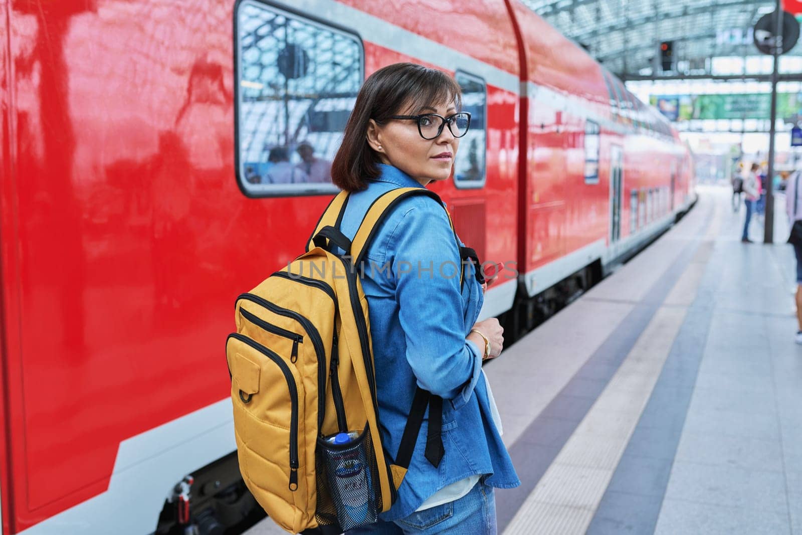 Woman waiting for railway public electric transport on platform of city station. Female with smartphone using banking app to buy online ticket payment, online timetable and route service, technology