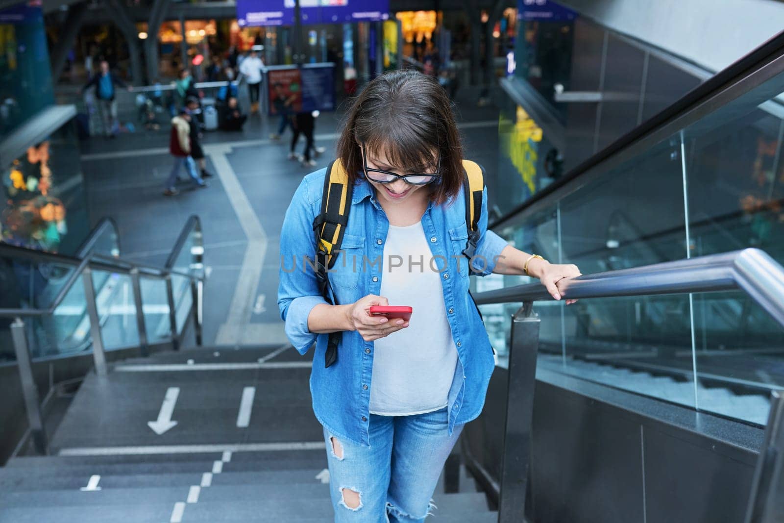 Woman on escalator stairs in building of city transport station with smartphone. Female using fast internet connection network for online ticketing service mobile application timetable transport route