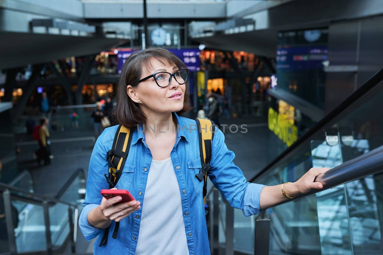 Woman on escalator stairs in building of city transport station with smartphone. Female using fast internet connection network for online ticketing service mobile application timetable transport route