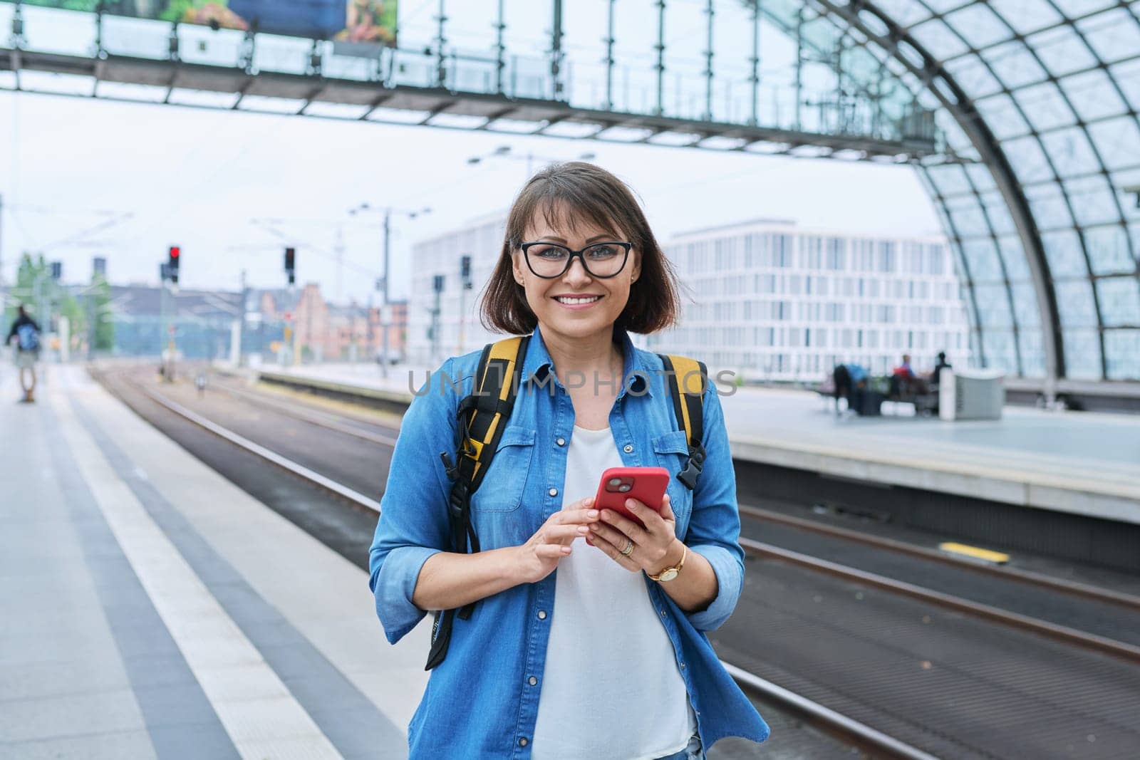 Mature happy woman looking at the camera inside the modern train station building by VH-studio