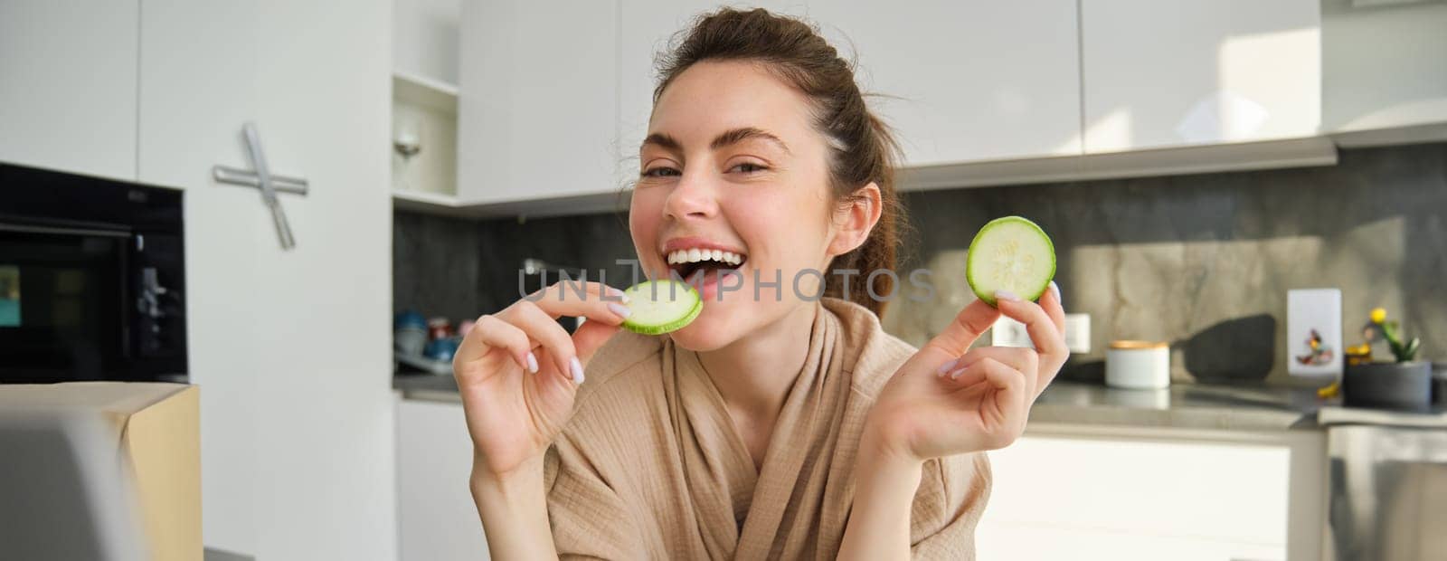 Portrait of happy, smiling young woman in the kitchen, cooking, chopping zucchini, holding vegetables and looking happy, preparing vegan food meal at home.