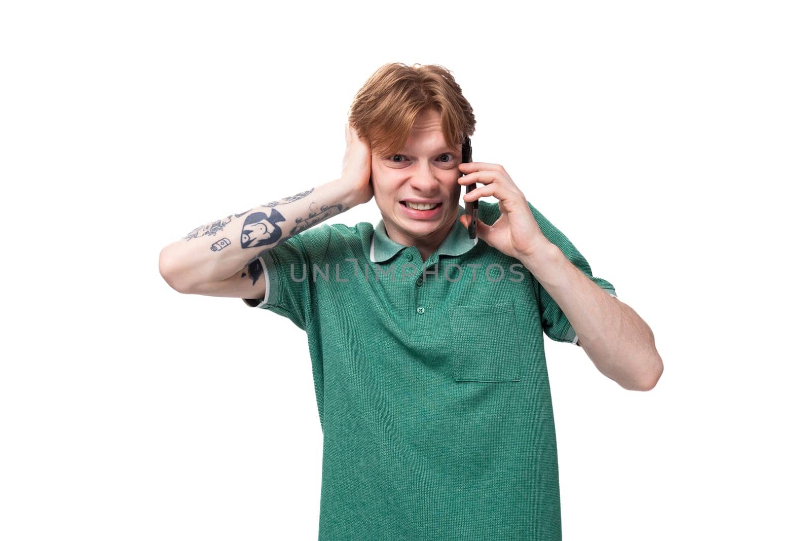 young charming adorable ginger man with a tattoo on his arm dressed in a green short sleeve t-shirt covers his ears with his hands by TRMK
