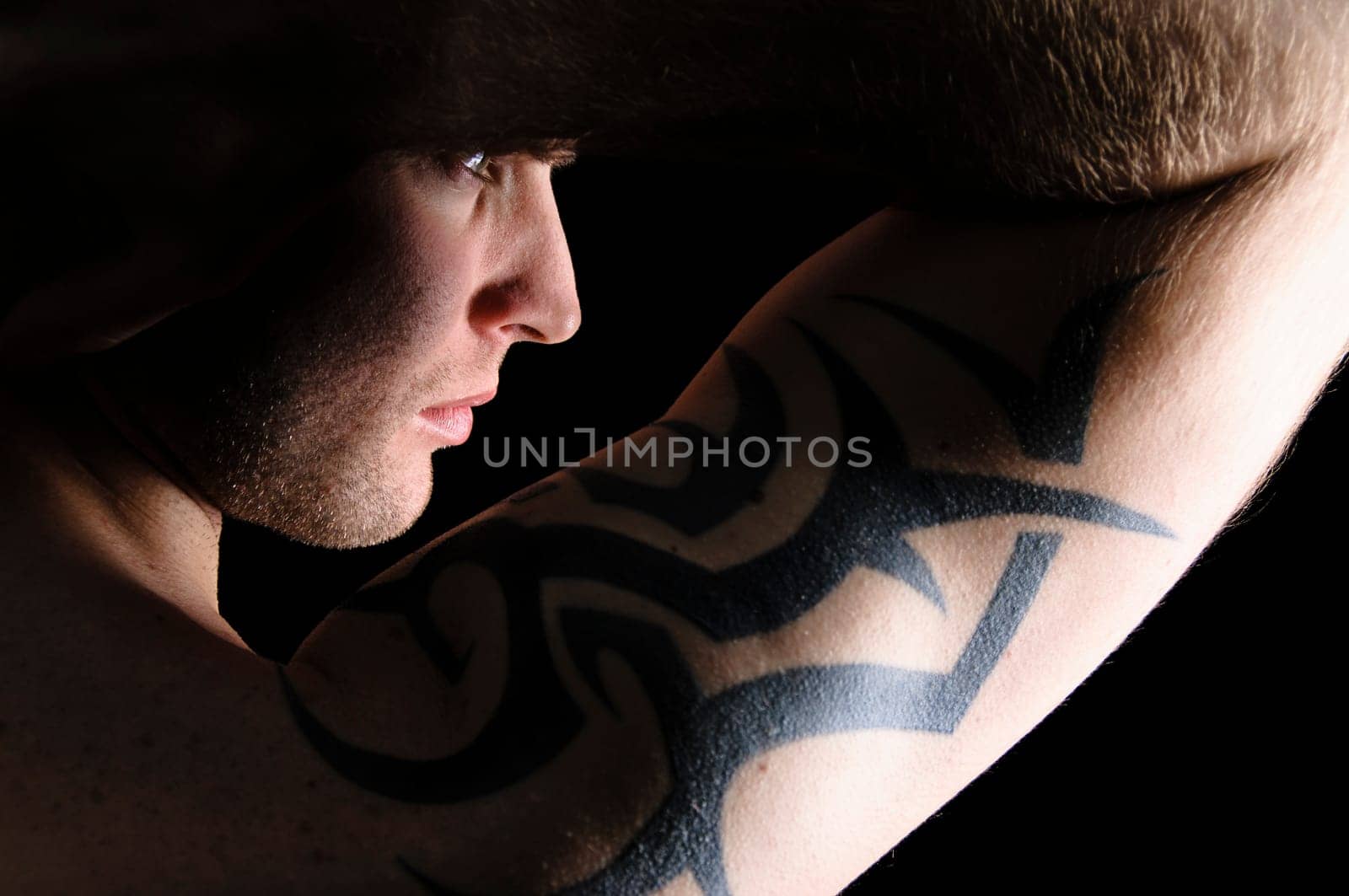 Young man showing his tribal tattoo on his shoulder, isolatad against black background.