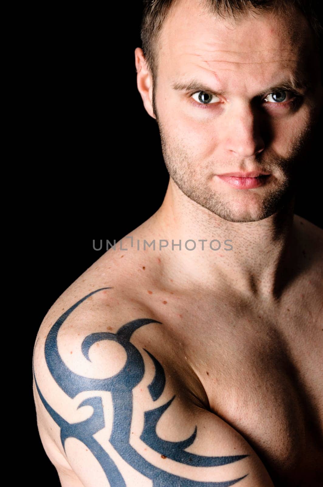 Young man showing his tribal tattoo on his shoulder, isolatad against black background.