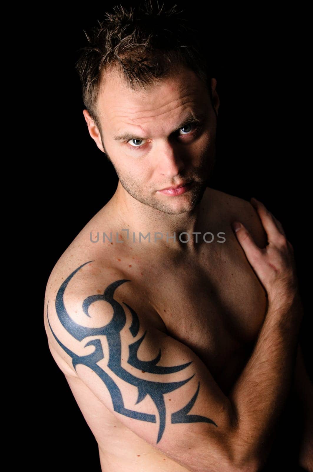 Young man showing his tribal tattoo on his shoulder, isolatad against black background.