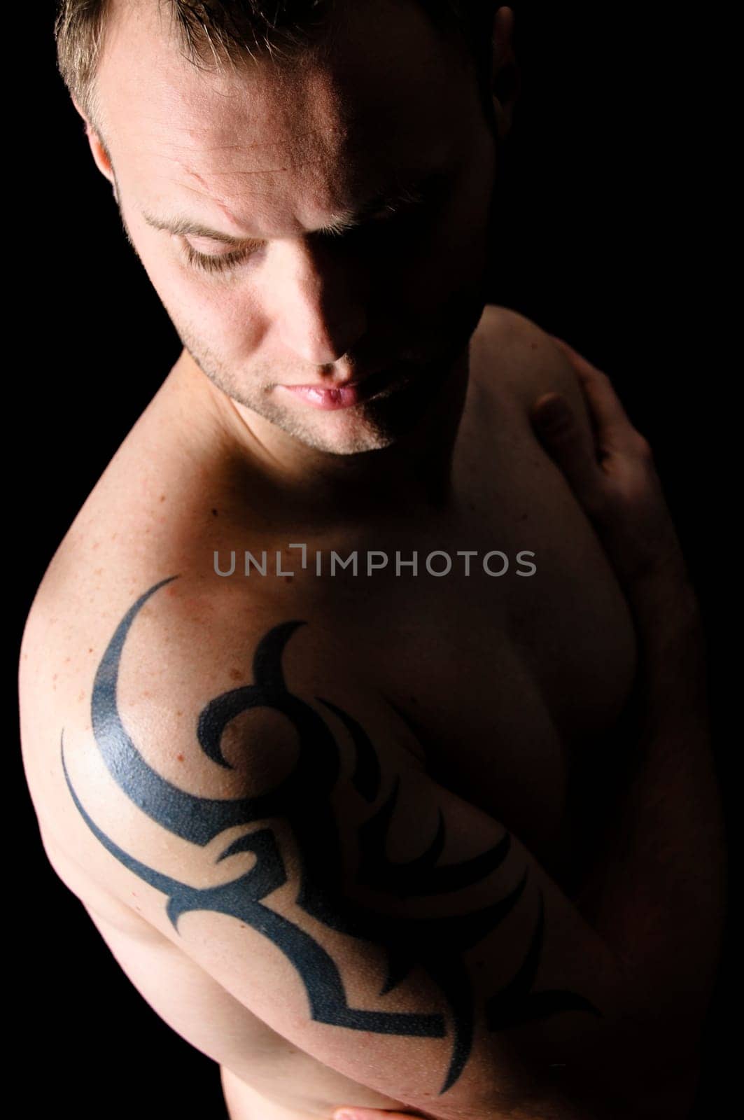 Young man showing his tribal tattoo on his shoulder, isolatad against black background.