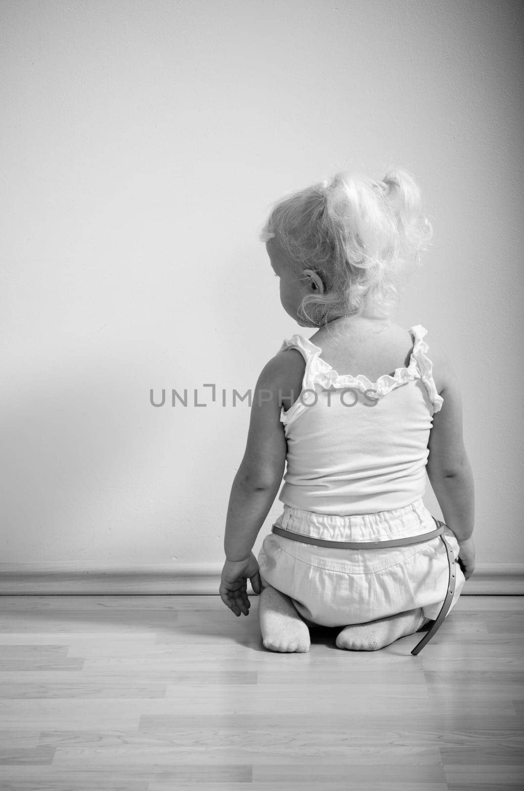 little girl sits on her knees facing the wall