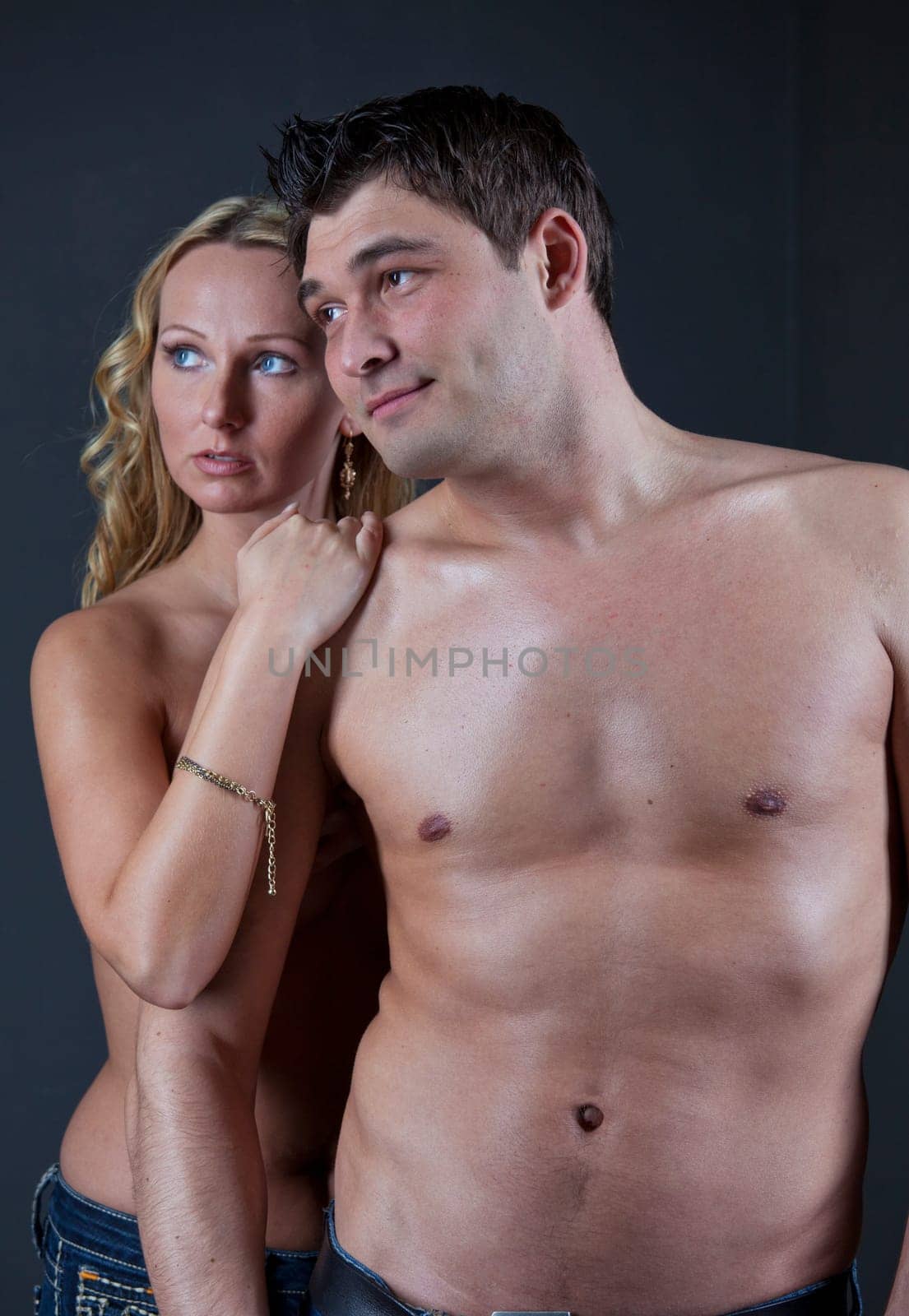 Portrait of Naked Couple embracing - shot in studio over grey background