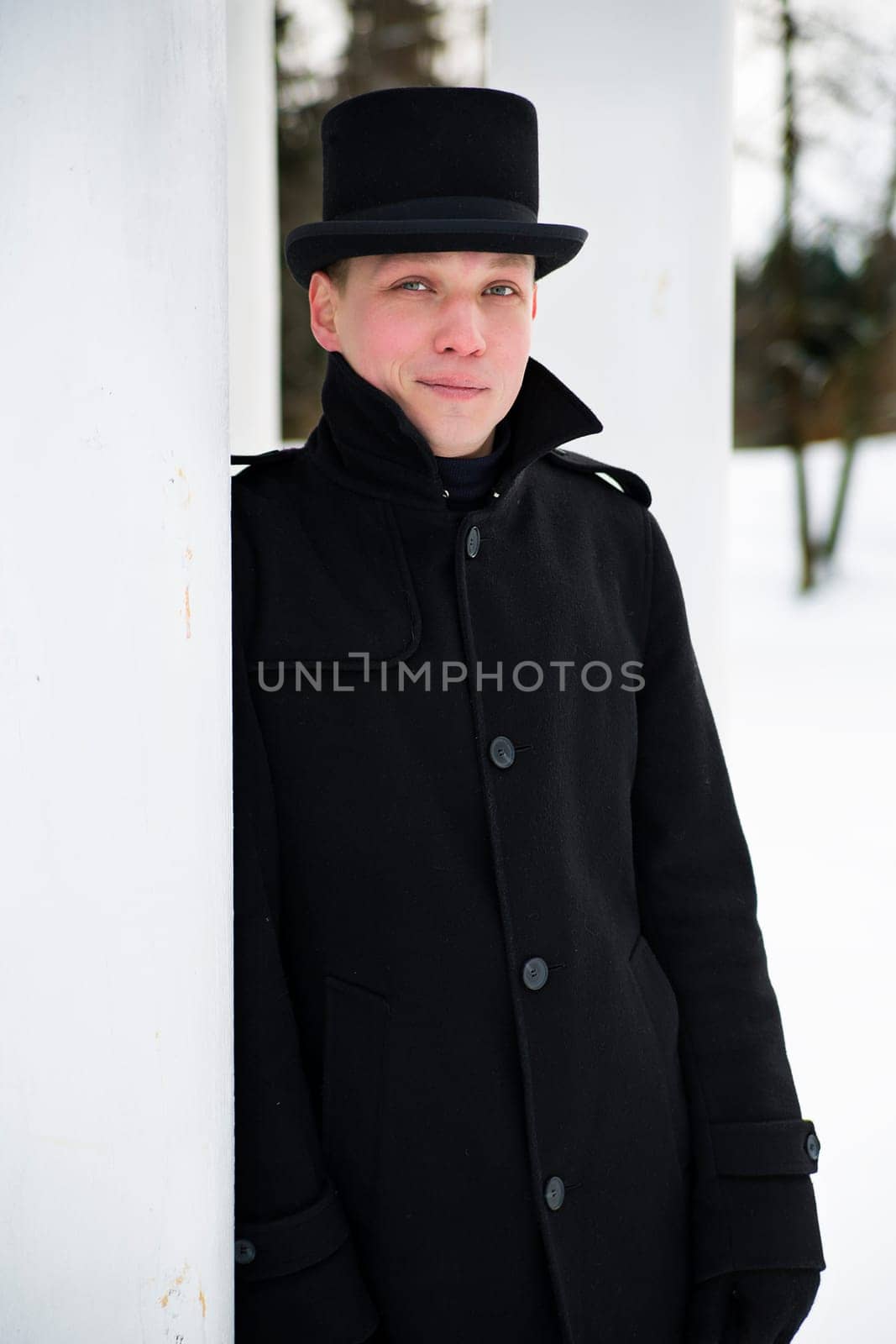 Young man in hat relies on white column