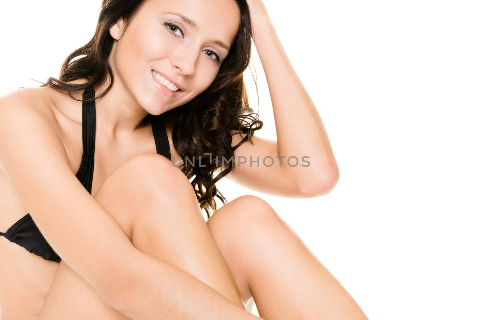 Young woman with black bikini sitting in front of white background