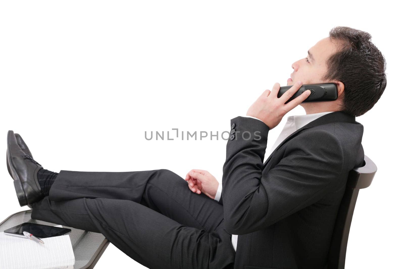 young business man relaxing at office desk and talking on mobile phone, isolated on white