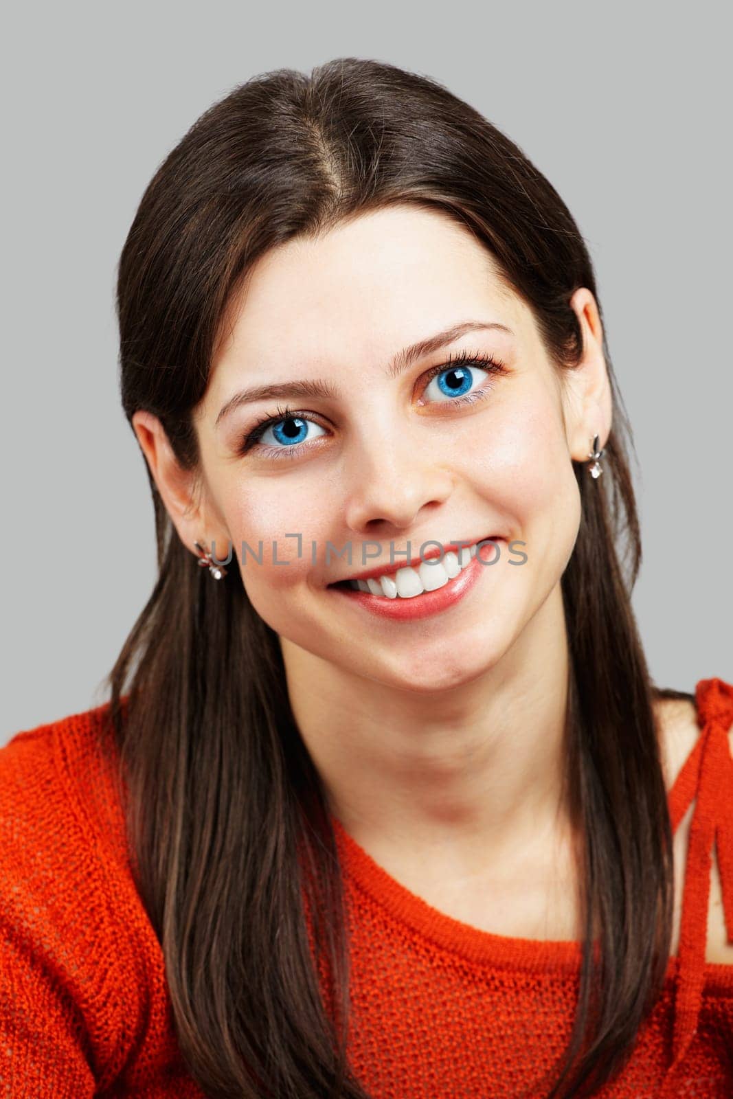 Portrait of a beautiful young woman smiling with red top over grey.