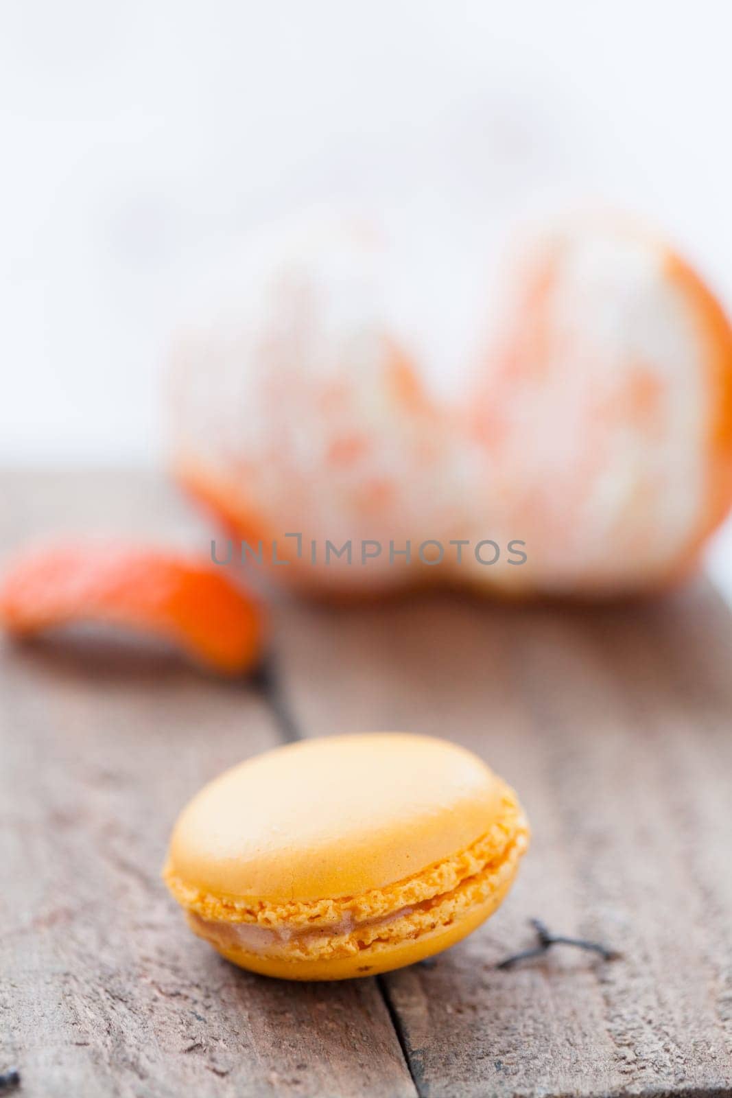 Closeup of yellow macaroon resting on wooden table with peeled orange in background