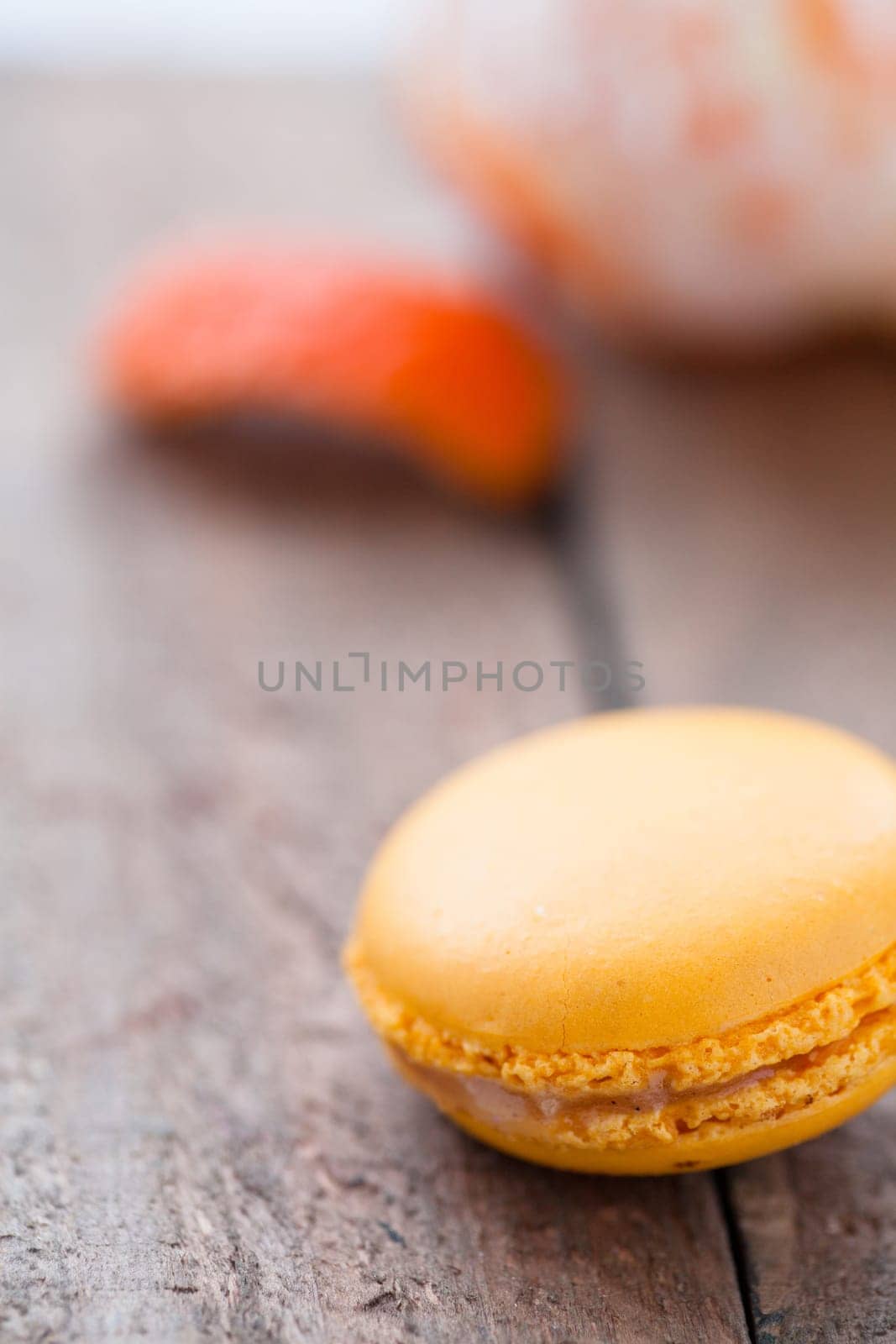 Closeup of yellow macaroon resting on wooden table with peeled orange in background