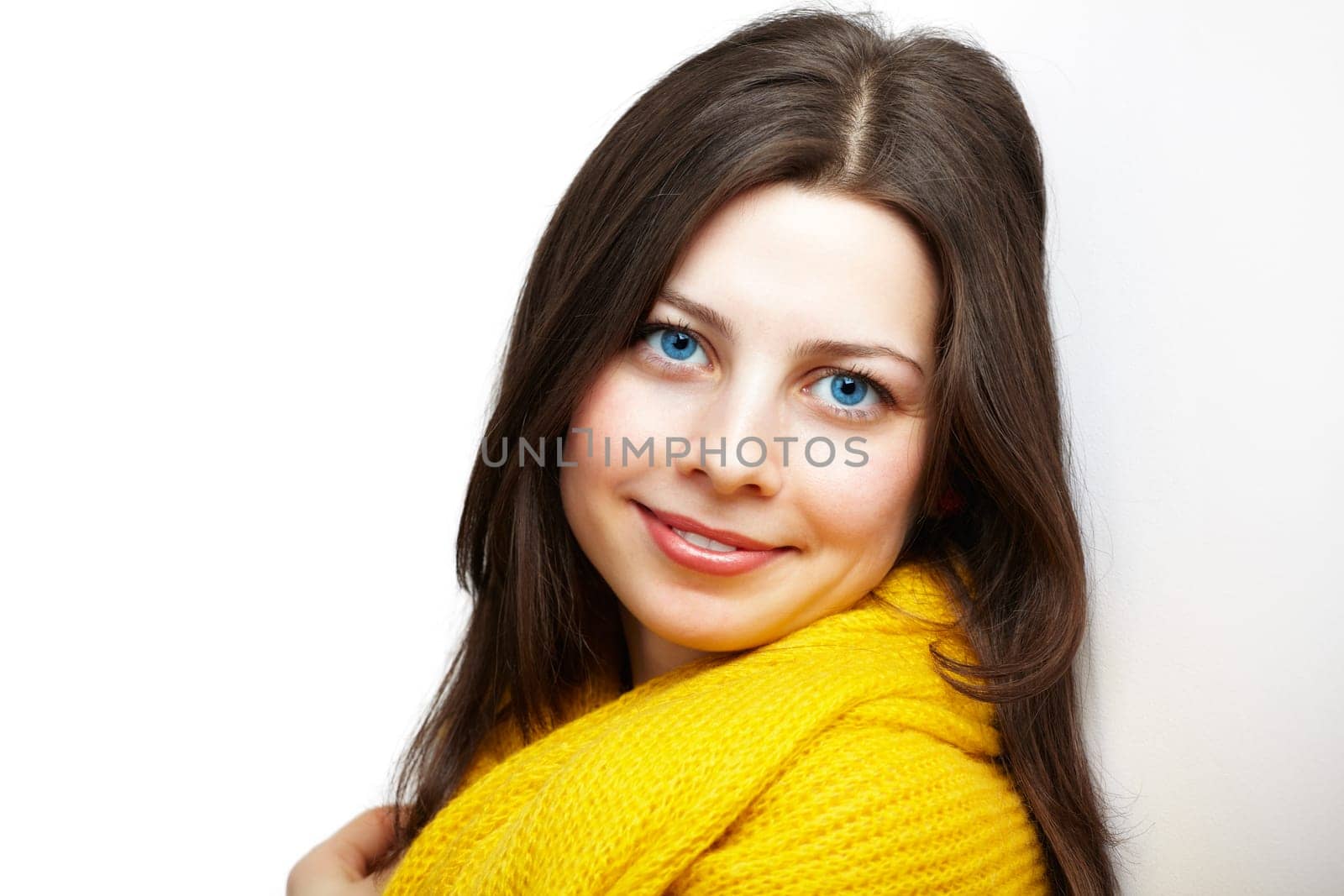 Portrait of a beautiful young woman with yellow scarf leaning against a white wall.