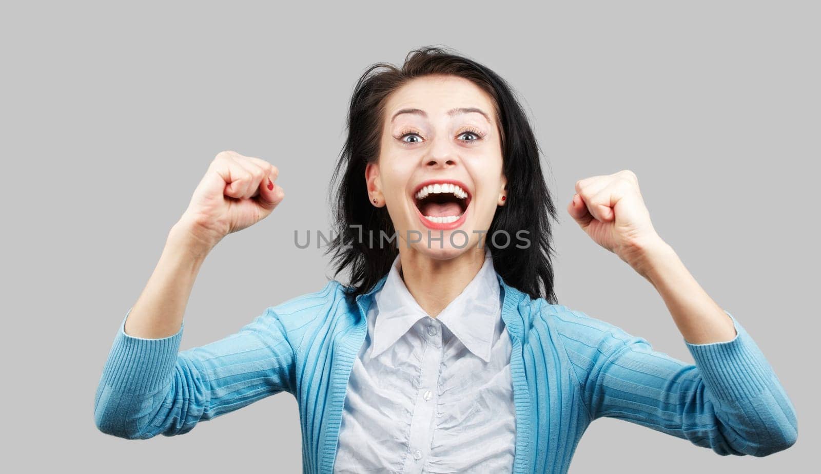 Portrait of a beautiful young woman excited with success over grey background.