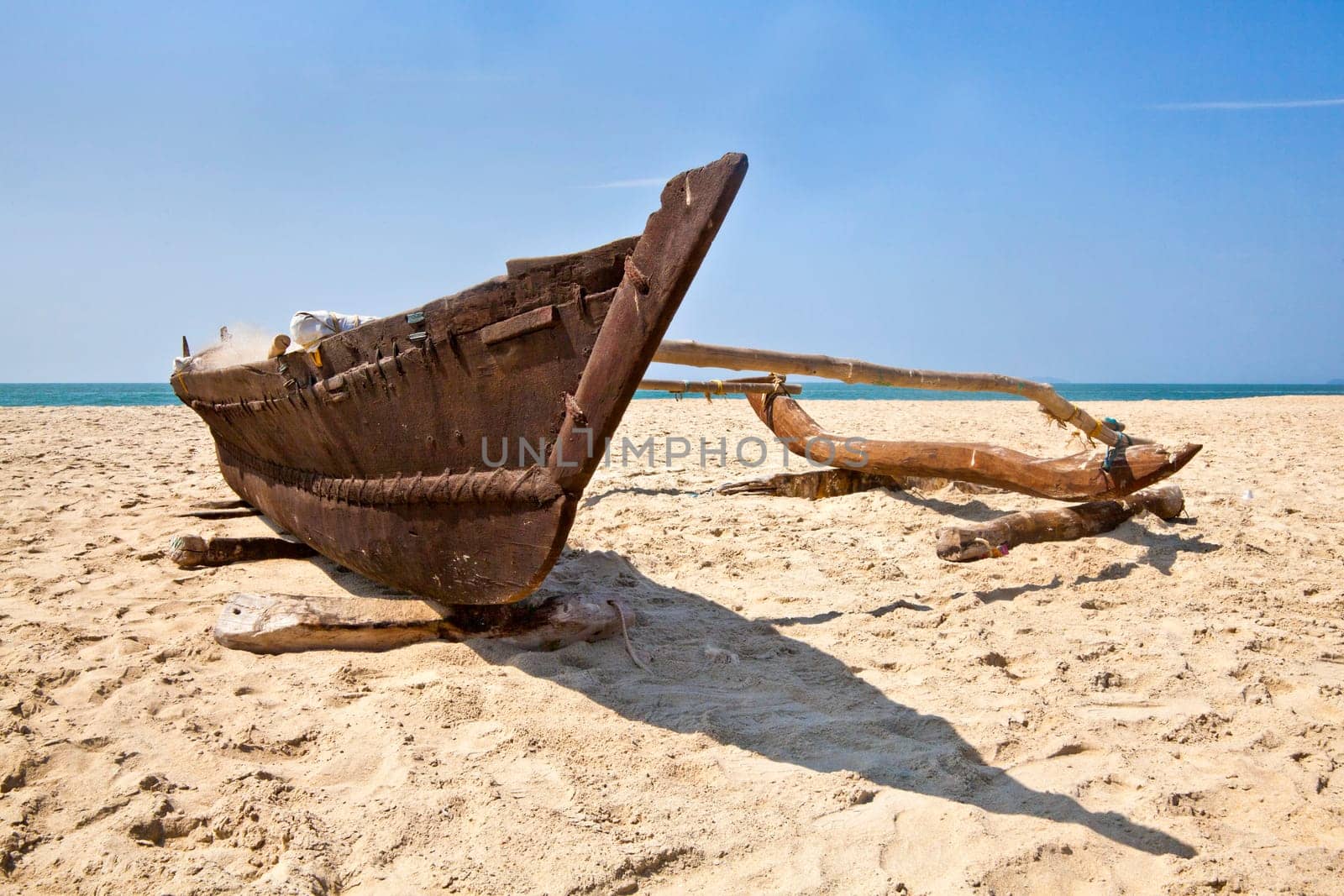 Landscape of a Goan secluded beach with shoreline, horizon and a fishermans catamaran single hull outrigger loaded with his working tools and tackle, Uttorda Beach, Goa, India