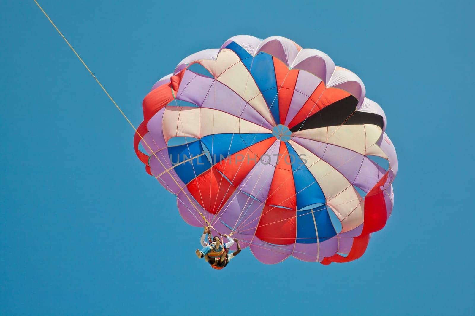 Horizontal landscape of a generic shot of asian paragliders flying tandem overhead in a clear blue sky. Image generated on Uttorda Beach, Goa, India, color, generic, holiday destination