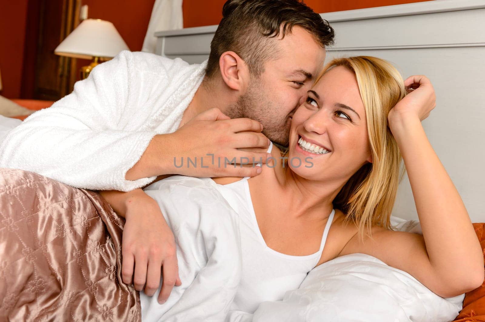 Happy couple in bed man giving kiss woman cheek