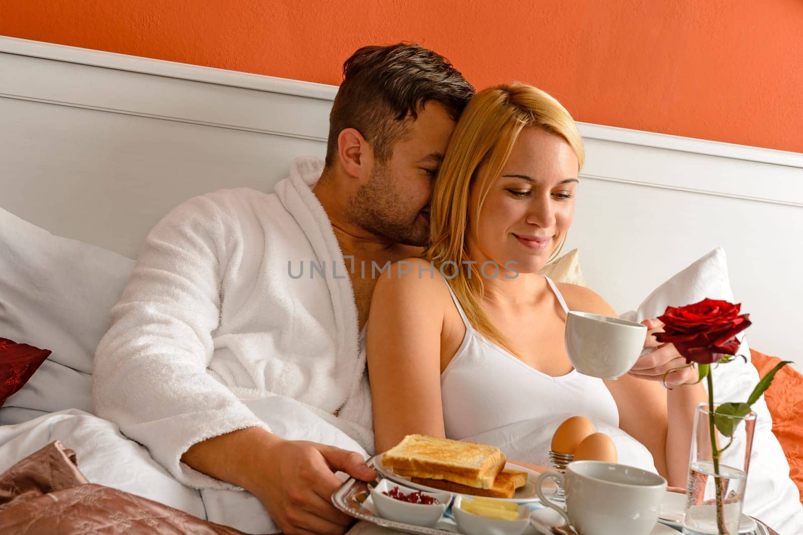 Cuddling young couple romantic morning in bed drinking coffee