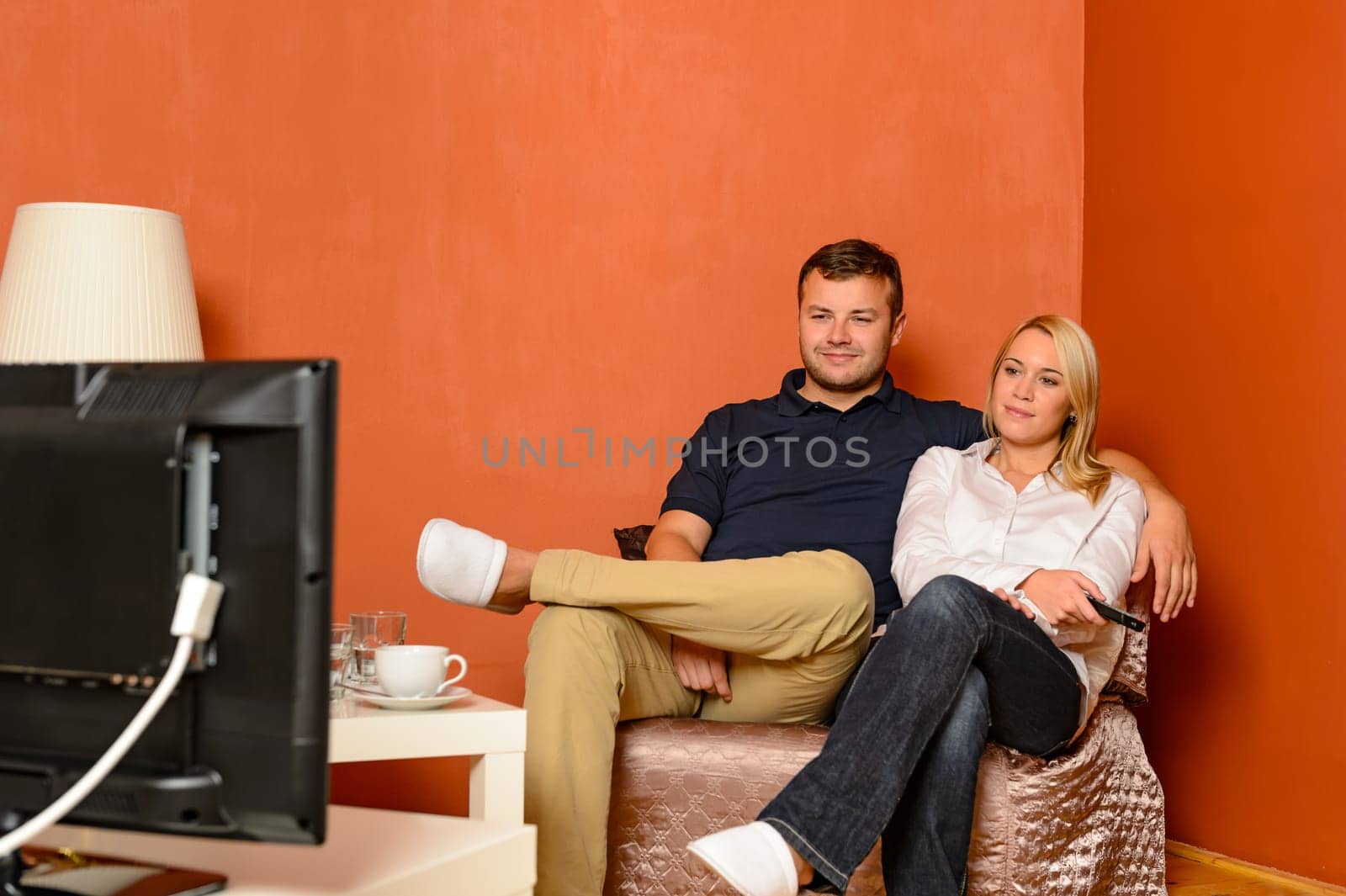 Young couple watching tv cuddling sitting armchair living room