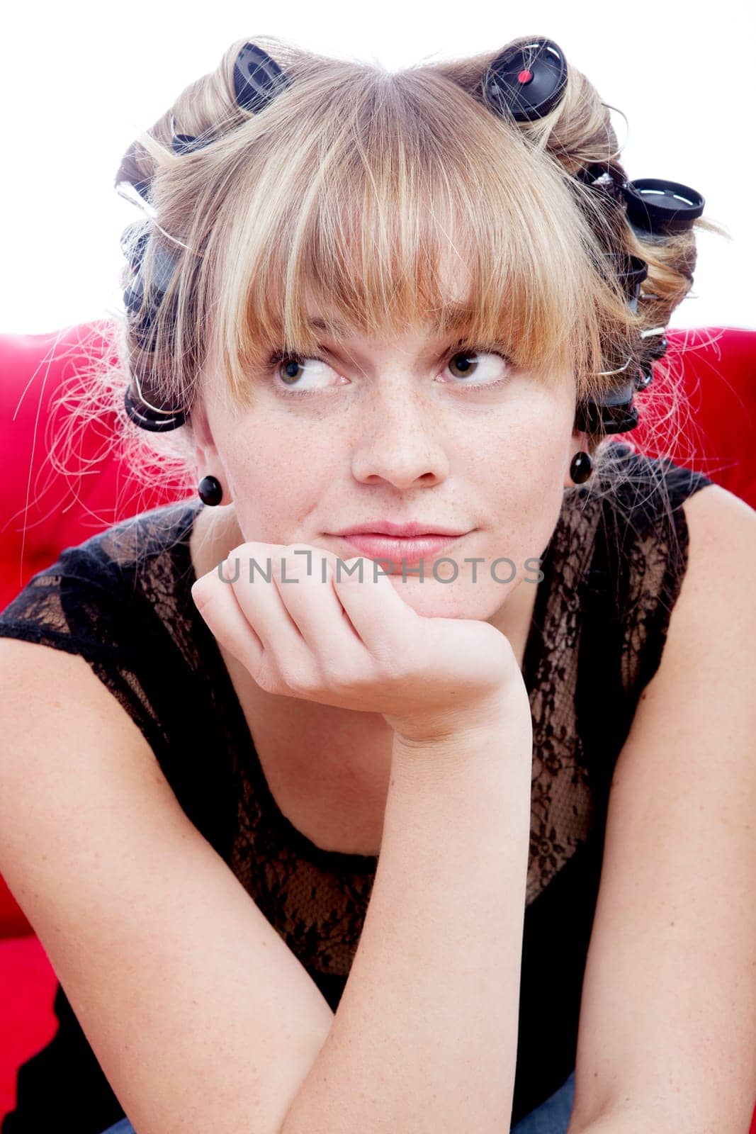 young blond girl sitting on sofa with curlers in hair on white background