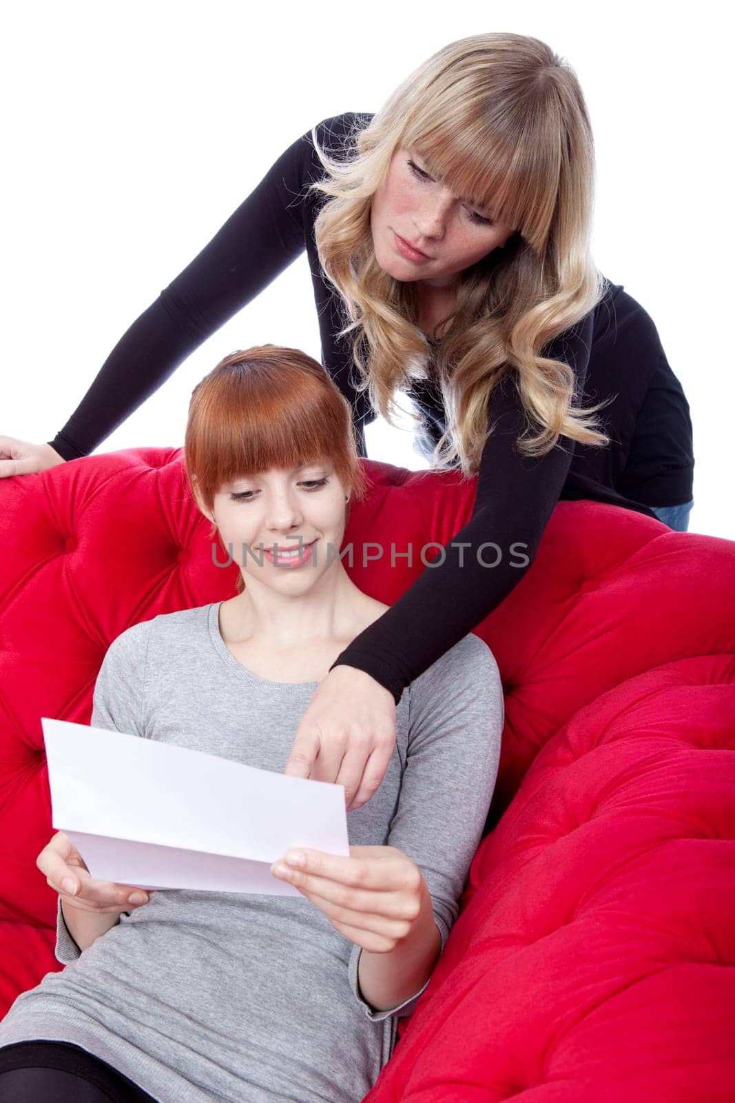 young beautiful blond and red haired girls on red sofa show letter in front of white background