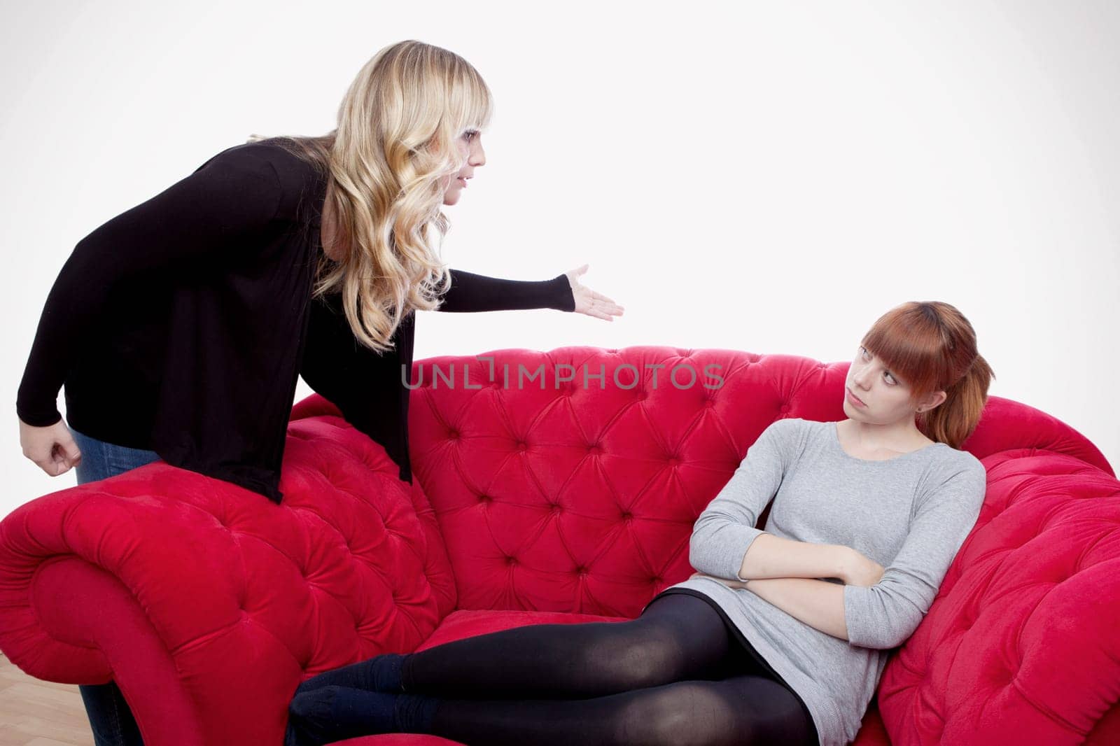 young beautiful blond and red haired girls have a fight on red sofa in front of grey background