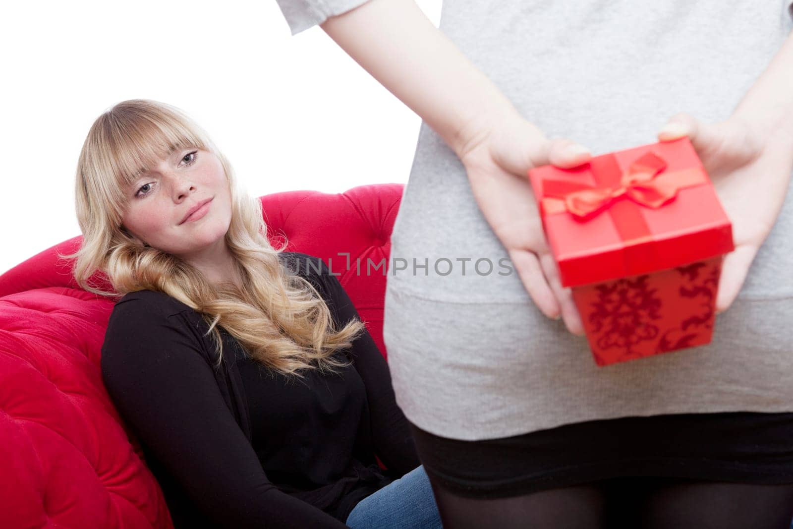 young beautiful blond and red haired girls on red sofa have a present box in front of white background