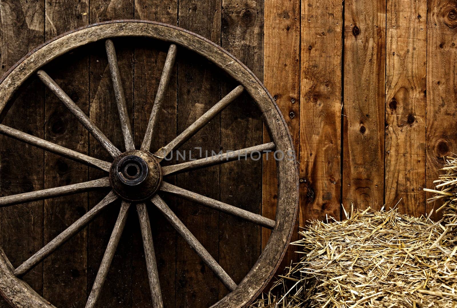 Vintage wooden carriage wheel, straw and wood background