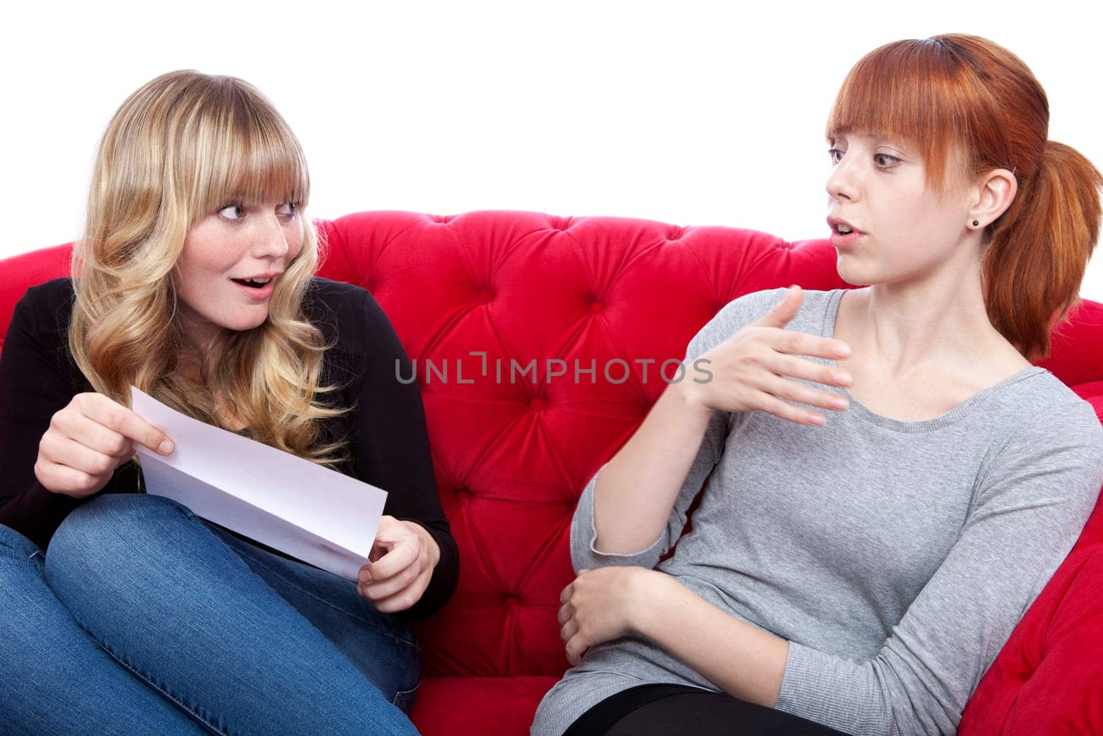 young beautiful blond and red haired girls on red sofa are excided about letter in front of white background