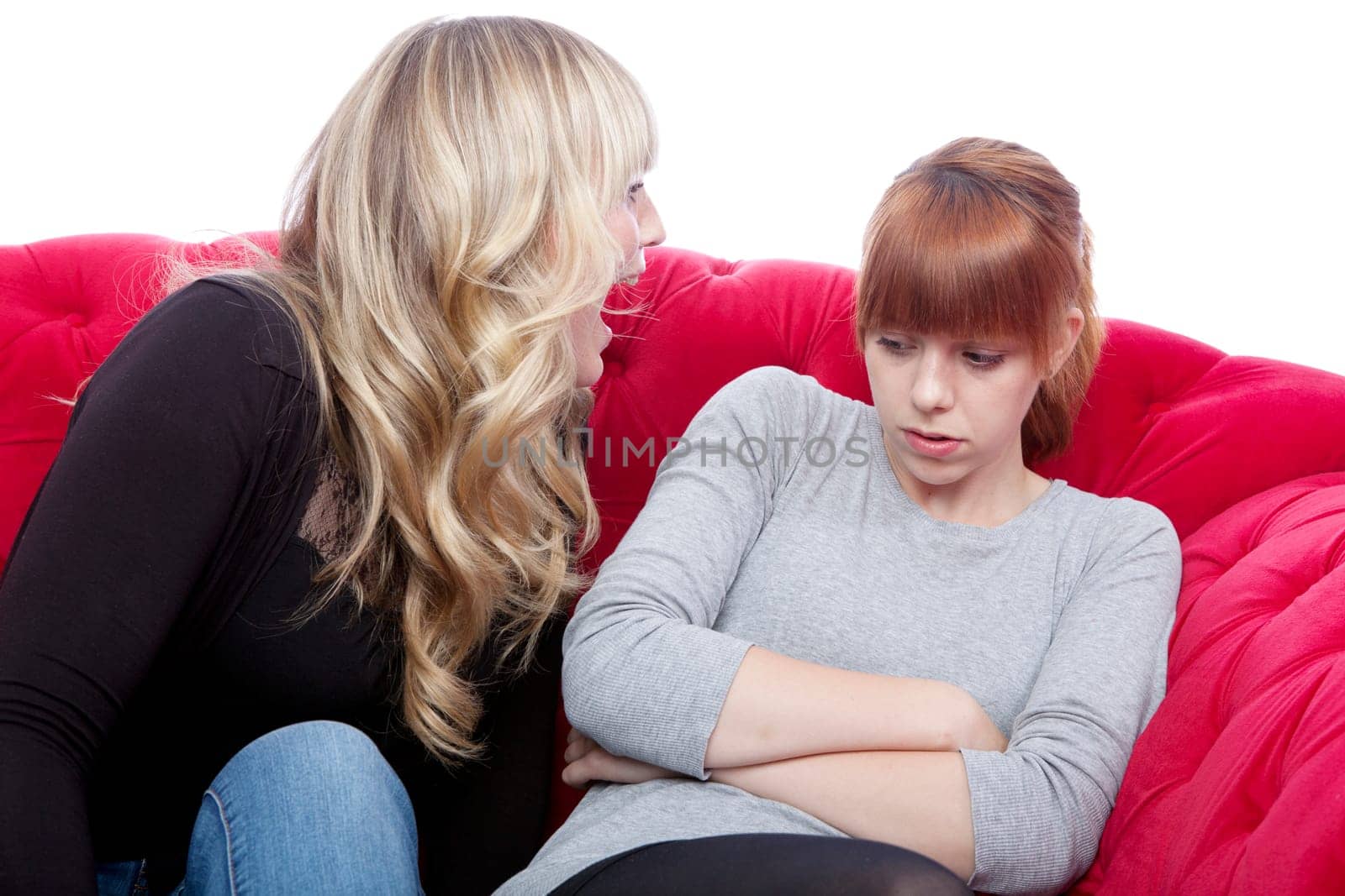 young beautiful blond and red haired girls on red sofa have a fight in front of white background