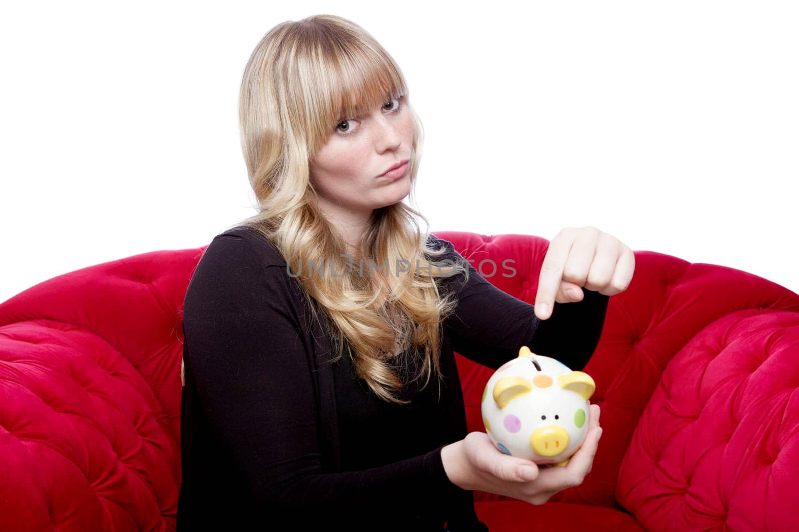 young blond haired girl want money in her piggybank on red sofa in front of white background